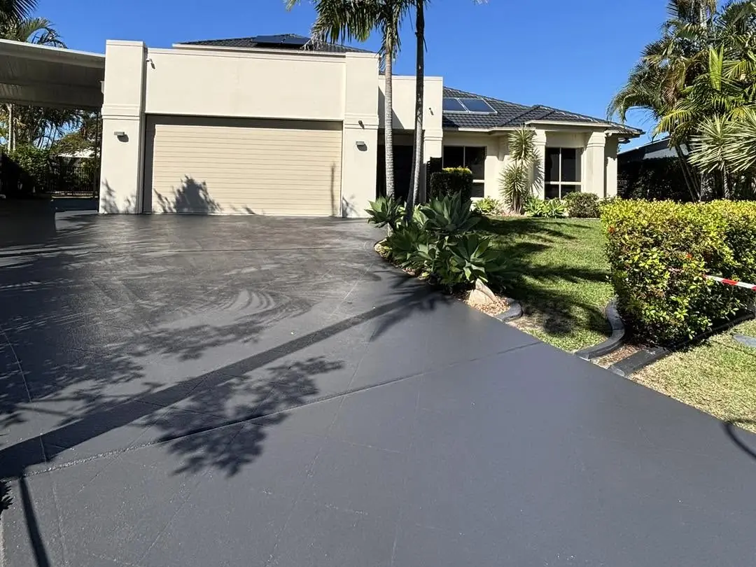 Front driveway re-coloured in charcoal, running up to a cream double garage under palm trees