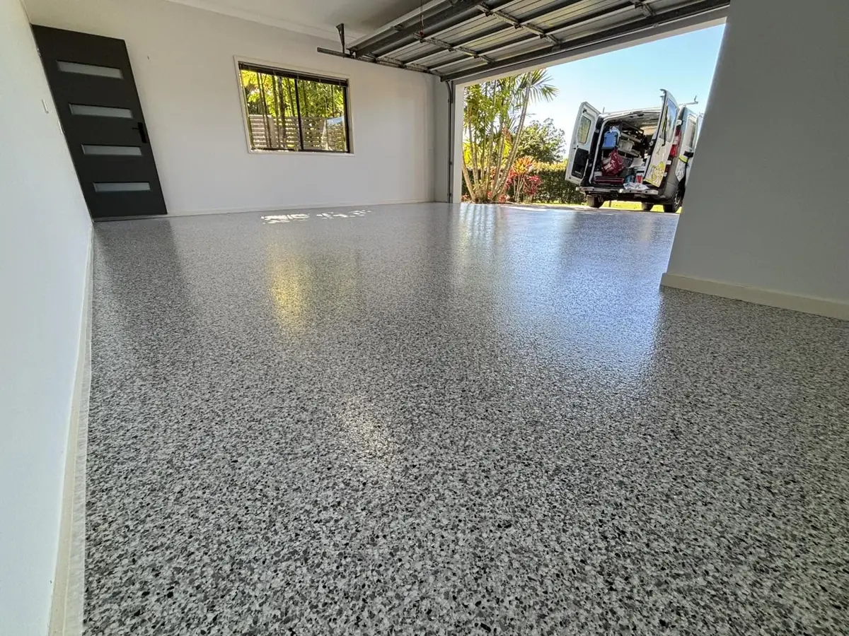 Double garage with a glossy grey epoxy flake floor, the roller door open to a van in the driveway