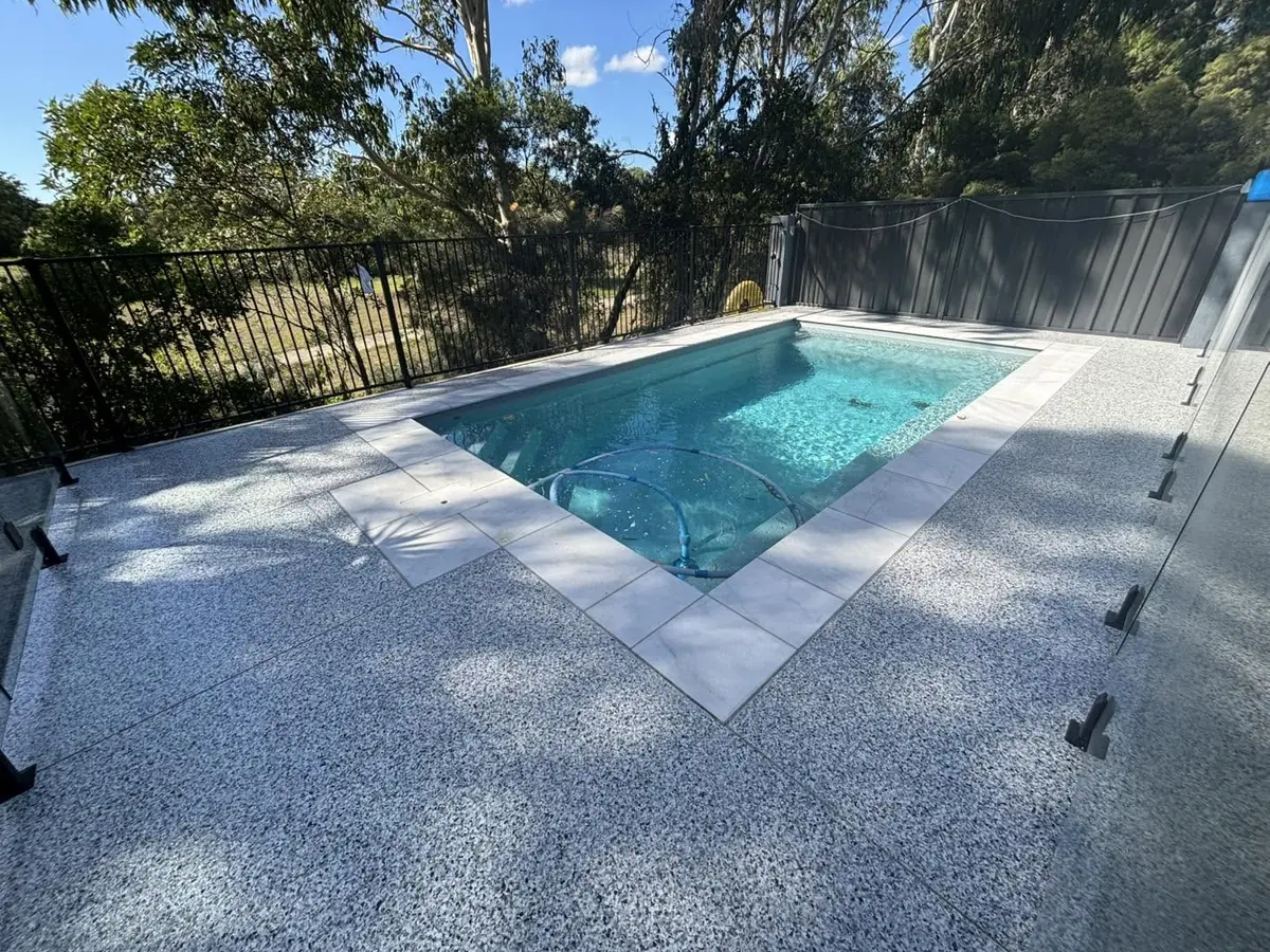 Pool surround with a speckled grey finish and pale coping, behind frameless glass pool fencing
