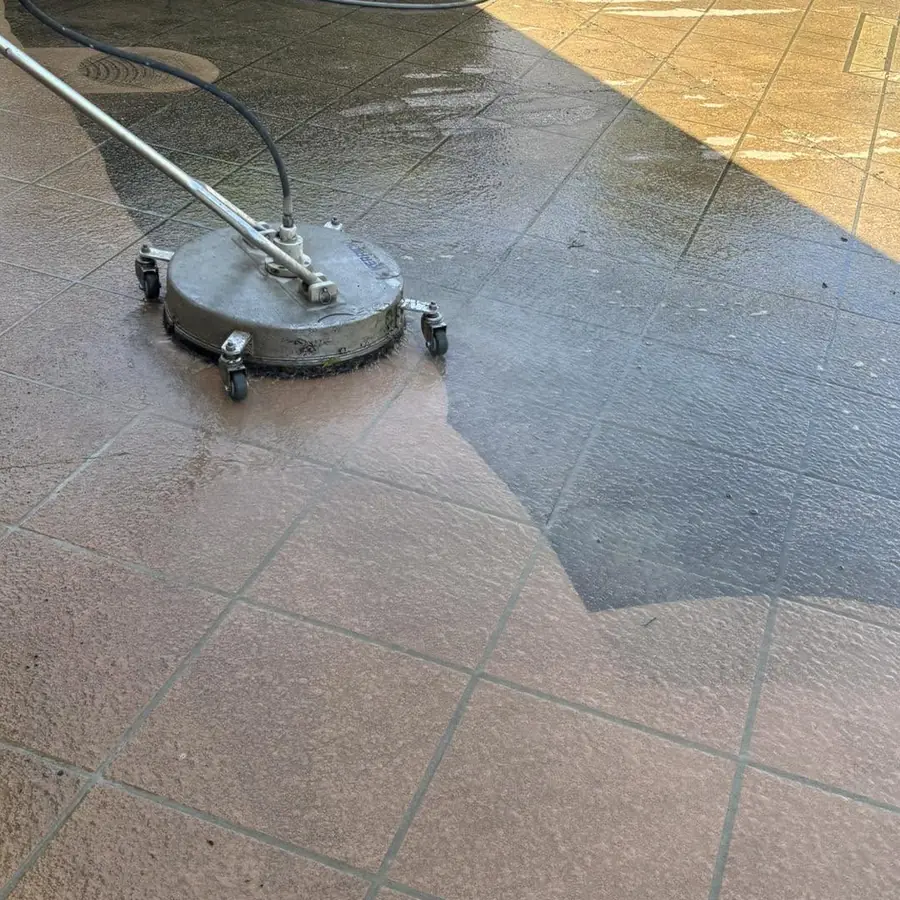 A rotary surface cleaner stripping years of grime off a stencilled concrete patio, the clean strip dark and wet beside the dusty surface