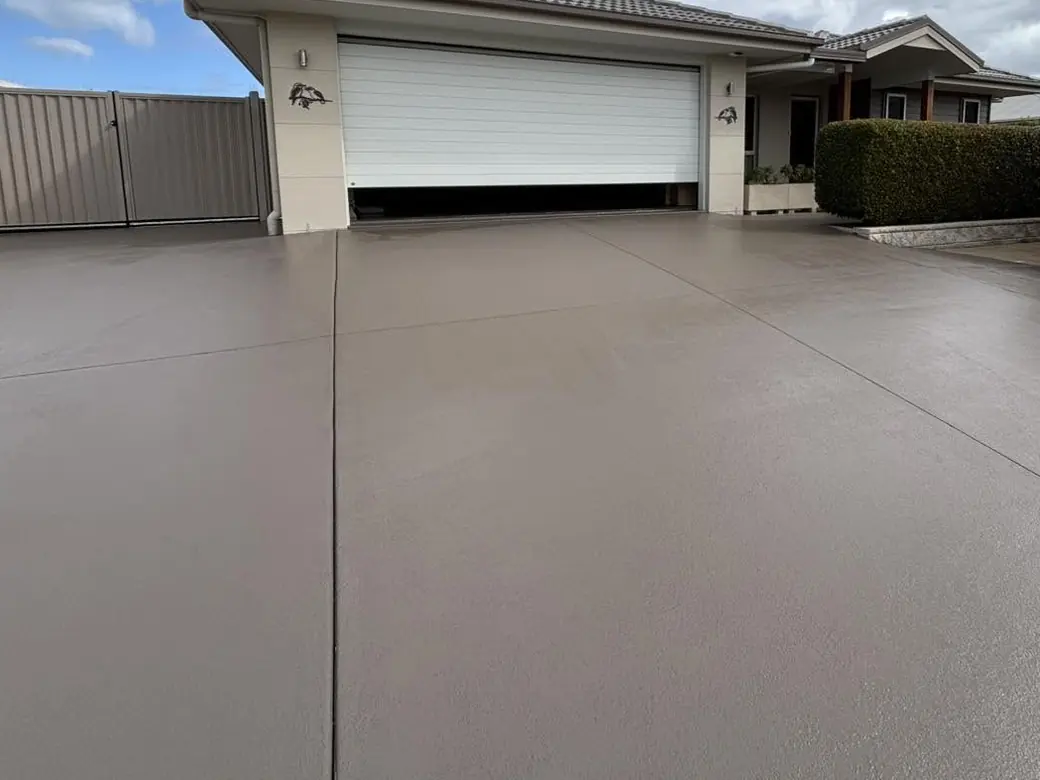 The same driveway after: one even, freshly sealed colour from the garage door to the kerb