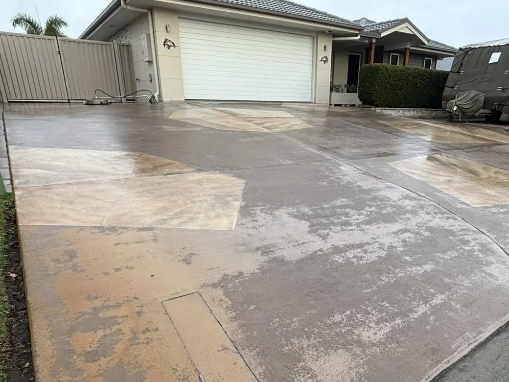 A front driveway before: washed-out, blotchy patches of old coating across the concrete
